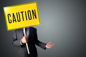 Businessman standing and holding a yellow caution sign in front of his head.jpeg Businessman standing and holding a yellow caution sign in front of his head.jpeg